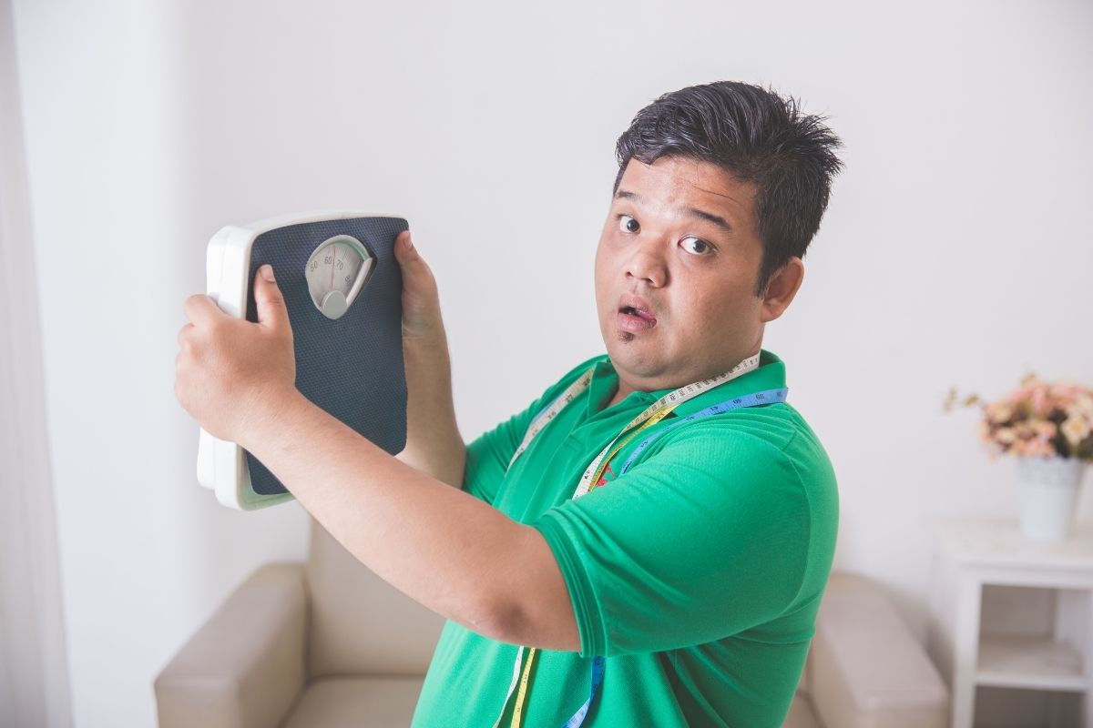 Seorang dengan berat badan berlebih membawa timbangan