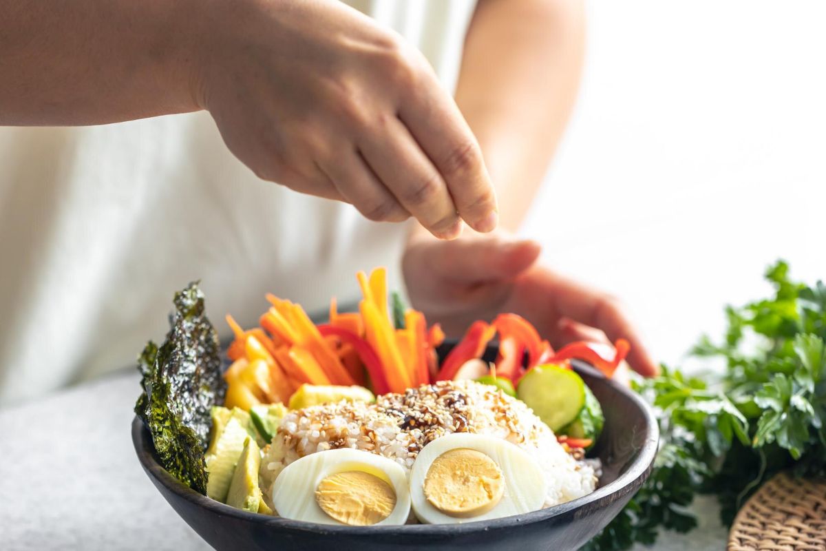 Seseorang sedang menyiapkan semangkuk nasi bercampur dengan sayuran dan telur