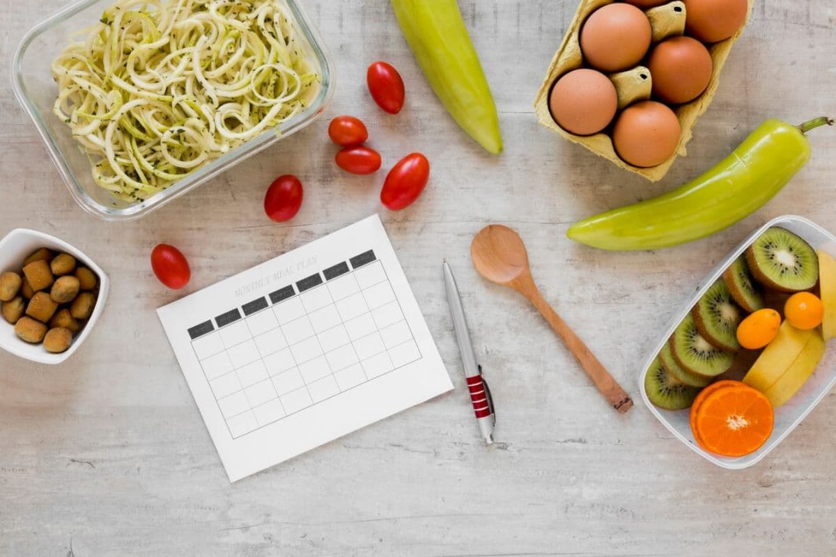 kertas, pulpen, sendok kayu, dan berbagai makanan sehat di atas permukaan datar